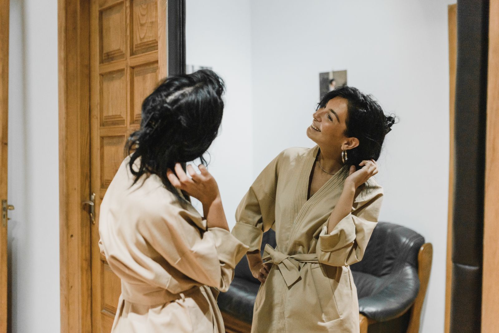 Woman smiling at her own reflection in the mirror, tying a beige robe