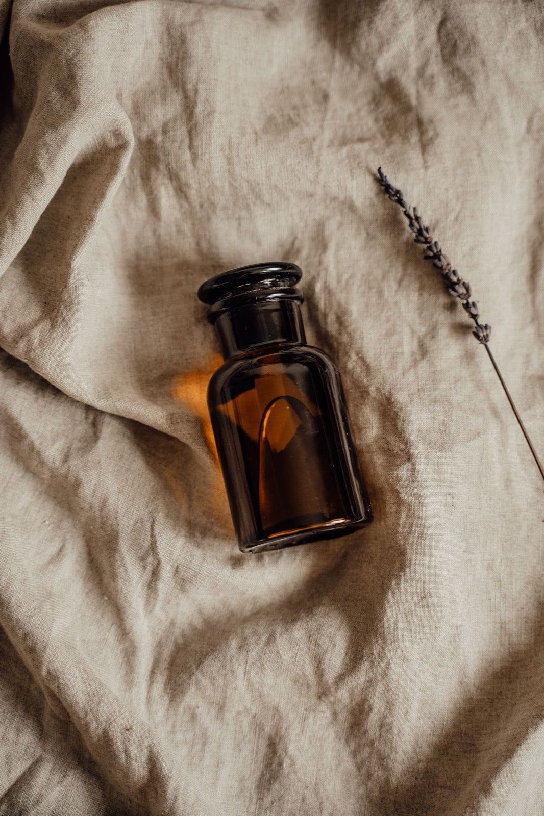 An amber glass bottle of intimate glide resting on warm linen in soft light