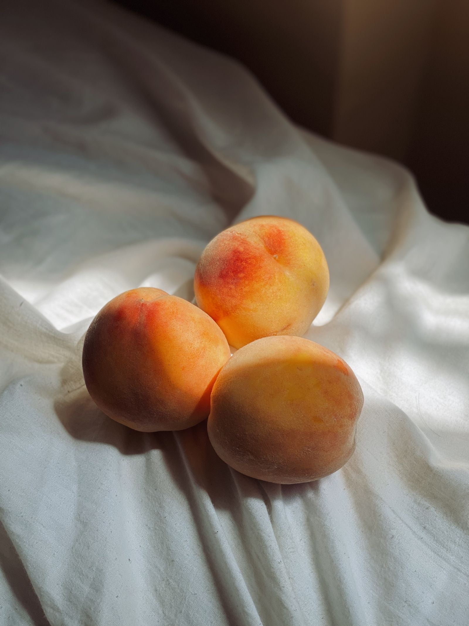 Three ripe peaches on linen in a strip of afternoon sun